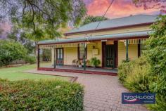  2965 Jacoby St Mundaring WA 6073 $1,000,000 In the heart of Mundaring, where the rhythm of modern life meets Western Australia’s pioneering past, stands a weatherboard and iron cottage that embodies the very essence of heritage living. Built circa 1901 by retired Bunbury harbour master Captain Thomas Scott, the remarkable “Stratheden” carries within its weatherboard walls the pioneering spirit that shaped early Western Australia. Hidden from the street by a charming picket fence and enveloped in lush, established gardens, this remarkable workers’ cottage offers a rare opportunity to inhabit a piece of living history whilst enjoying the unparalleled convenience of one of the region’s most coveted locations. 3 bedrooms 1 bathroom 1901 weatherboard & iron Striking workers’ cottage Extensive Jarrah panelling Wide jarrah floorboards High pressed metal ceilings Rear lane access to garage Estab gardens, bore retic 2023 sqm heart Mundaring Steps to Trail, park, village The extensive use of jarrah throughout this property immediately distinguishes it as a superior example of vernacular architecture, where wide floorboards and striking panelling speak to the craftsmanship and material abundance of a bygone era. Here, the integrity of the original fabric has been meticulously preserved, creating an authentic connection to the past that is increasingly rare. This is not simply a house that has been renovated; it is a heritage treasure that has been lovingly maintained, telling the story of Western Australia’s timber heritage. The approach to the home sets the tone for what lies beyond – a wide, bullnose verandah extends a gracious welcome, while pressed glass in subtle pastel hues surrounds the front door like jewels set within a frame. Living here means beginning each day with this gentle beauty, where morning light filters through coloured glass and the established gardens create a private sanctuary mere steps from Mundaring’s vibrant village centre. Upon crossing the threshold, the significance and integrity of this property become immediately apparent through the soaring ceiling, its pressed metal painted white, creating a striking vertical dimension that speaks to the generous proportions seen throughout the home. Picture rails and wide jarrah floorboards create a striking welcome that sets expectations high, and the home delivers on every promise. The entrance hall is flanked by two generously proportioned bedrooms, each graced with original windows, pressed metal ceilings and decorative fireplaces. At the end of the hallway, a pair of interior doors open to reveal the property’s masterpiece – a living room that embodies an authentic and uniquely Western Australian aesthetic. Vertical jarrah boarding rises to dado height, and horizontal panelling continues to the jarrah-clad ceiling. An expanse of eight-paned windows draws northern light into the heart of the home, creating a space where the seasons become part of daily life, where winter afternoons glow golden against the jewel-toned timber and summer mornings arrive soft and bright. Living in this room means inhabiting a space where craftsmanship and comfort converge, where every surface speaks to the skill of builders who understood both beauty and function. At one corner of this magnificent living space, a breakfast nook provides an intimate setting for morning rituals, whilst the kitchen represents a faultless melding of history and modern convenience. The original chimney breast and hearth, fitted with a Metters stove, anchor the space with authentic period detail, while pressed metal and jarrah panelling blend seamlessly with gold-flecked stone benchtops, under-bench cabinets, and contemporary appliances, including a freestanding electric oven and dishwasher. This kitchen exemplifies how heritage properties can incorporate modern elements without compromising their character. The principal bedroom, accessed via the living room, offers generous proportions. High ceilings ensure an airy, relaxed atmosphere that transforms sleep into restoration, whilst a separate walk-in robe and dressing room provide practical luxury. Reverse cycle air conditioning delivers year-round comfort, demonstrating that while heritage is honoured, contemporary expectations for comfort are uncompromised. Spanning the rear of the plan, a sunroom with a swathe of windows looking out to the rear garden creates a seamless connection between indoor and outdoor living. Terracotta floor tiles ground the space in earthy authenticity, while reverse-cycle air conditioning and direct access to both the rear garden and an alfresco entertaining zone ensure this bright space suits year-round use. A family bathroom and well-appointed laundry at either end of the sunroom complete the thoughtful arrangement of spaces. The transition to outdoor living occurs through French doors that connect the sunroom to a large, crazy-paved patio set beneath a wisteria-threaded pergola – a space where entertaining becomes effortless and where the changing seasons provide an ever-evolving backdrop. Living here means experiencing the joy of alfresco dining where privacy and tranquillity coexist with incredible accessibility to village amenities. The current owner’s dedication as a skilled and passionate gardener has created botanical magic that transforms this property from merely impressive to utterly enchanting.  Bore reticulated lawns and gardens cocoon the outdoor living spaces, creating profound privacy and calm despite the home’s remarkably central location. Camellia, deciduous trees, and hardy native plants create a tapestry of colour, texture, and seasonal interest that rewards close observation and daily enjoyment. Practical considerations have not been overlooked – rear lane access leads to a powered garage and a remarkable railway carriage studio, a two-room space complete with verandah that offers endless possibilities for creative pursuits, home business ventures, or simply a peaceful retreat. A small garden shed and single carport enhance the home’s practical amenities. The location represents perhaps the property’s greatest triumph – positioned mere steps from the Sculpture Park and Heritage Trail, with the shops and services of Mundaring Village within comfortable walking distance. Schools, sporting facilities, and public transport networks are all within easy reach of this hidden oasis, creating a lifestyle where convenience never requires compromise of character or tranquillity. Living here means enjoying the best of both worlds: the peace of established gardens and heritage architecture, paired with the vibrancy and accessibility of one of the Hills’ most desirable communities. True luxury lies in authenticity, craftsmanship and connection to place. Here, in this superior example of vernacular architecture, surrounded by a mature garden landscape and positioned in Mundaring’s coveted heart, the past and present converge to create something genuinely extraordinary. 
